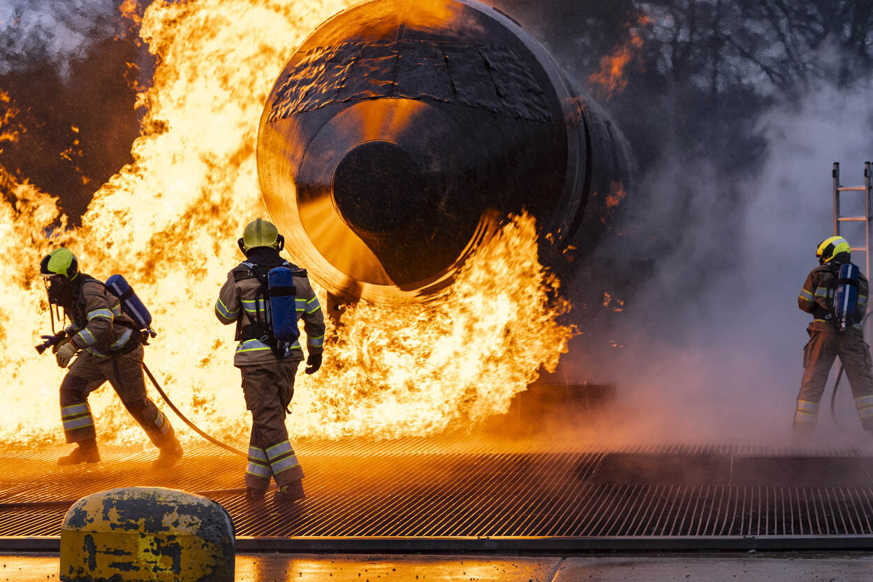 Enorme felgele en oranje vlammen schieten uit de mock-up van een verkeersvliegtuig met op de achtergrond gitzwarte rookwolken.
