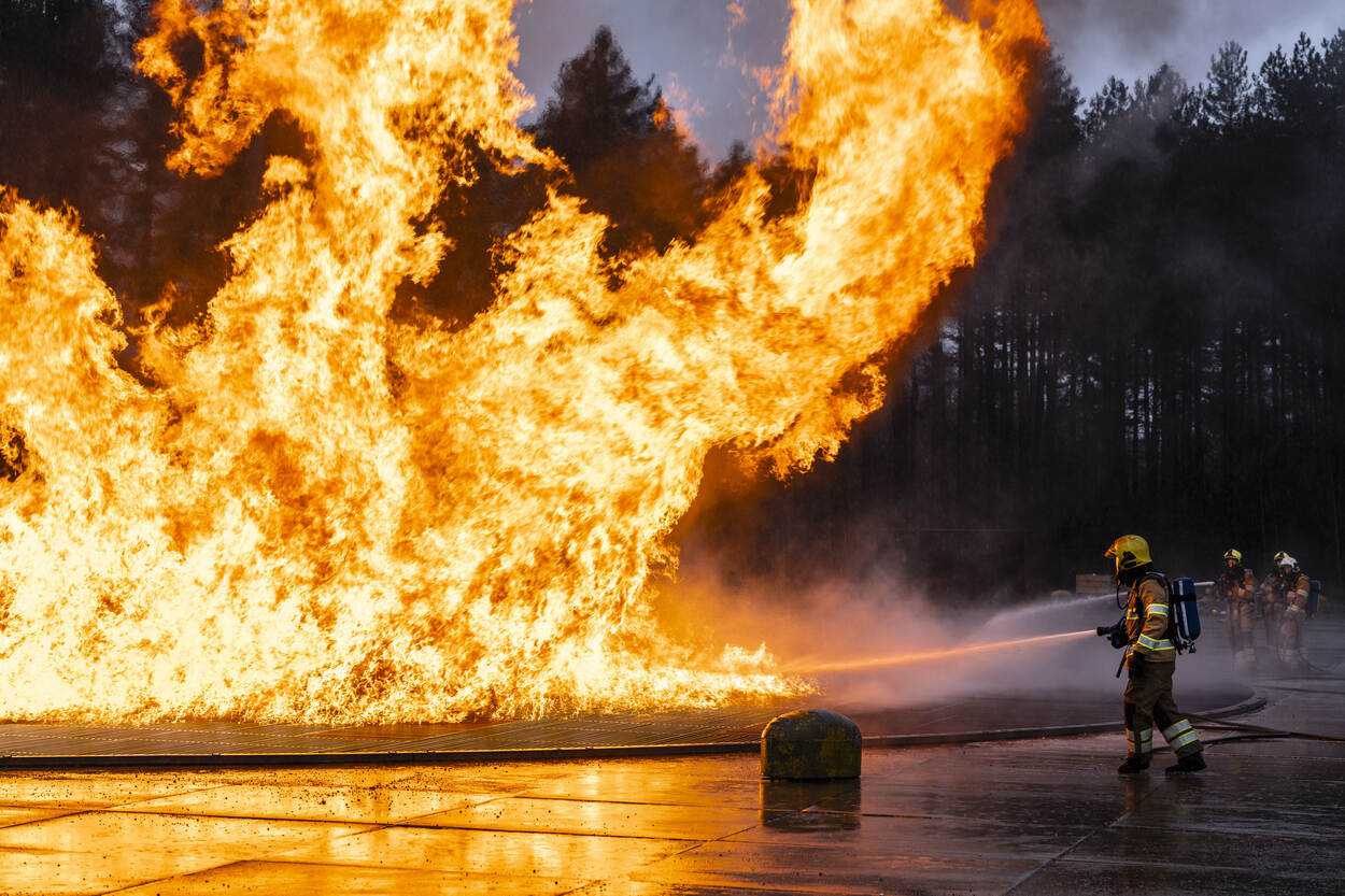 Enorme felgele en oranje vlammen schieten uit de mock-up van een verkeersvliegtuig met op de achtergrond gitzwarte rookwolken.