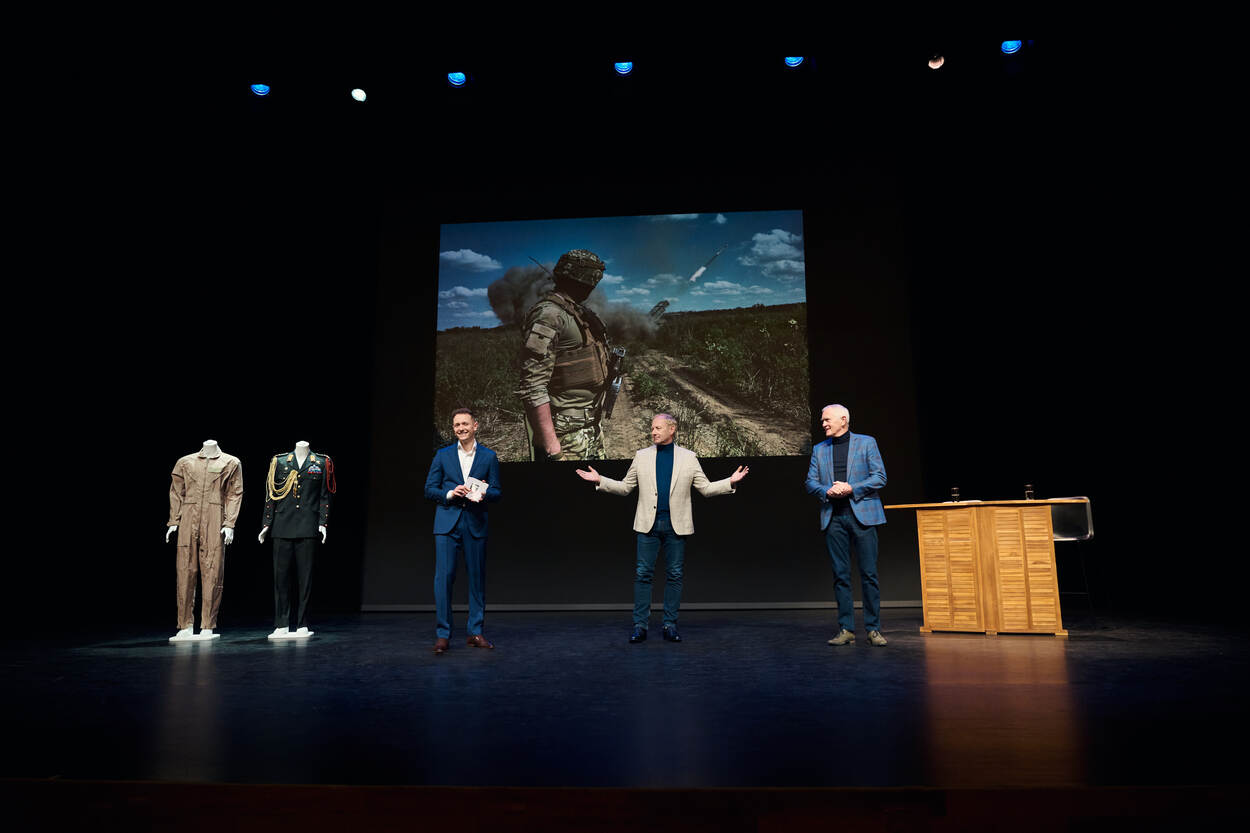 Foto genomen van het podium, met daarop Van Uhm, De Kruif en journalist Jos de Groot.