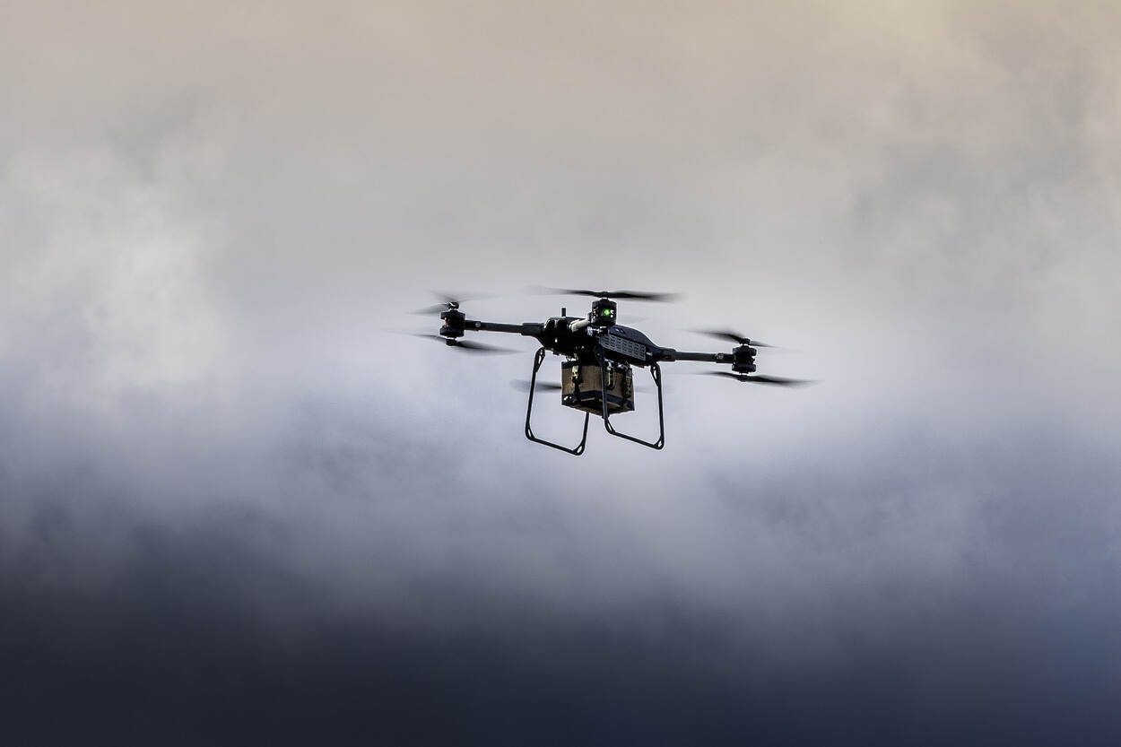 Een drone vliegt door de lucht. Daaronder hangt een klein pakketje, de cargo.