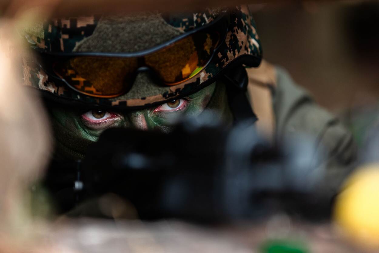 Een gecamoufleerde Oekraïense militair tuurt het voorterrein in, met een wapen voor zijn gezicht.