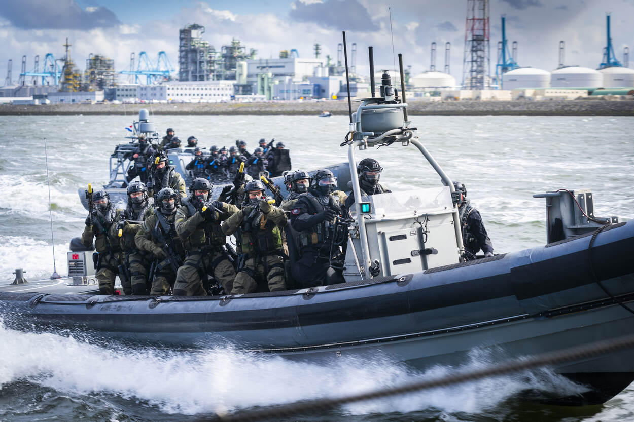 Mariniers op een snel varende boot voor de haven van Rotterdam. Allen dragen ze een lang wapen. De zon schijnt. Een balaclava voor het gezicht maakt de militairen onherkenbaar.
