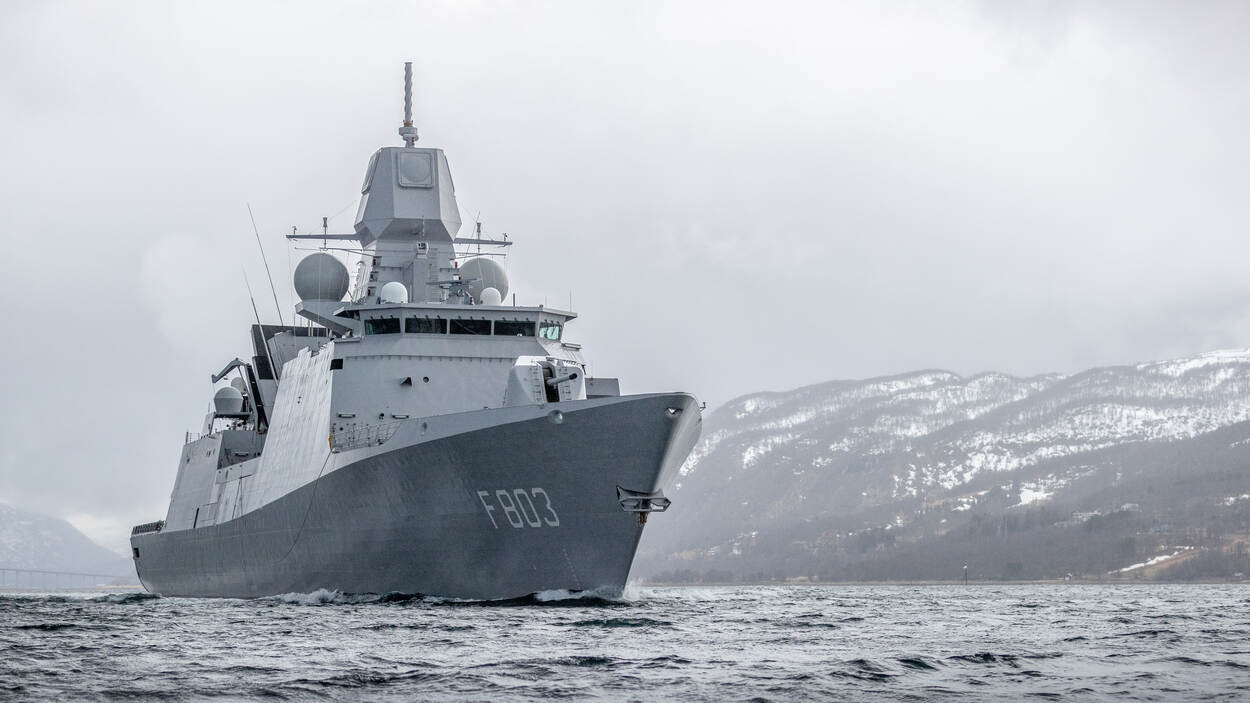 Een marineschip op zee, met op de achtergrond besneeuwde heuveltoppen.