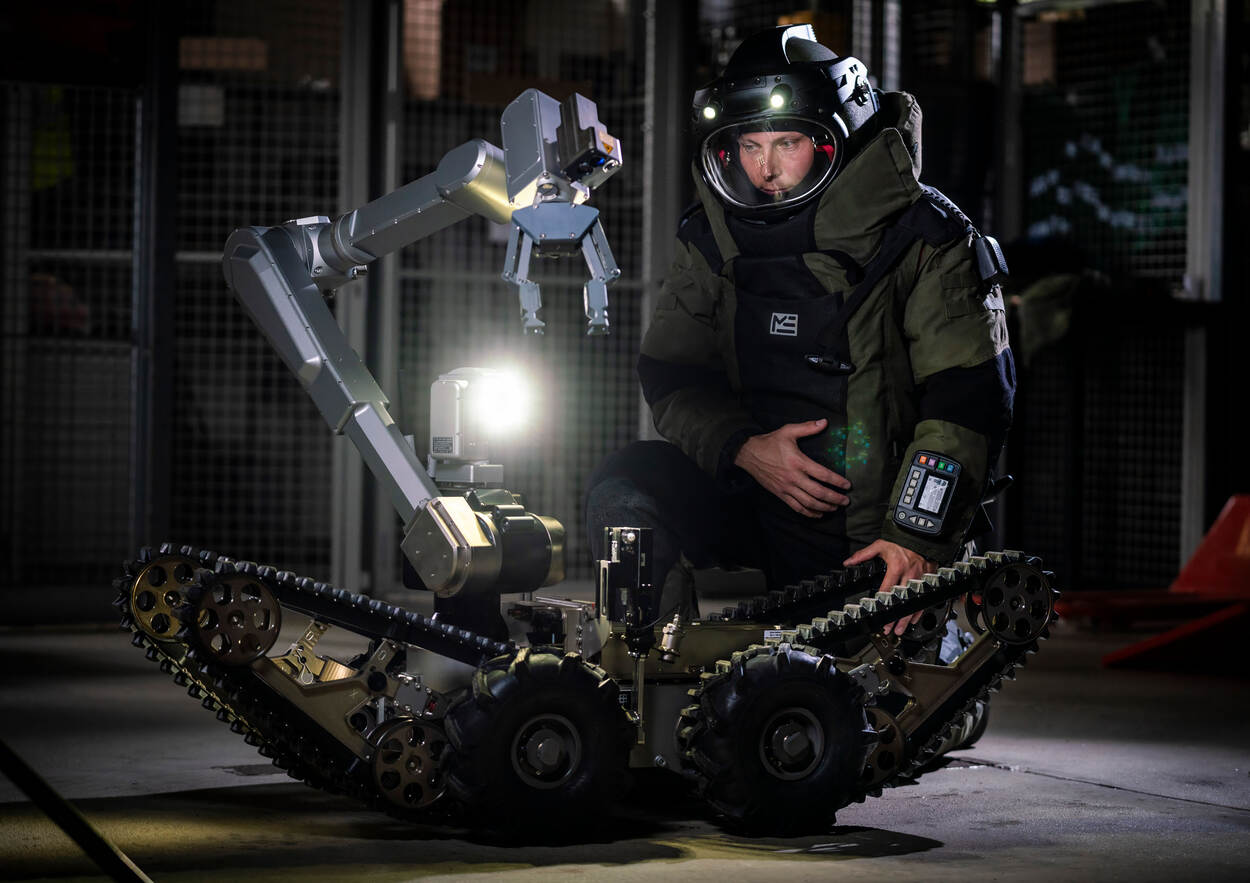 Een EOD-medewerker in bompak zit achter een speciale robot waarmee verdachte pakketjes worden onderzocht.