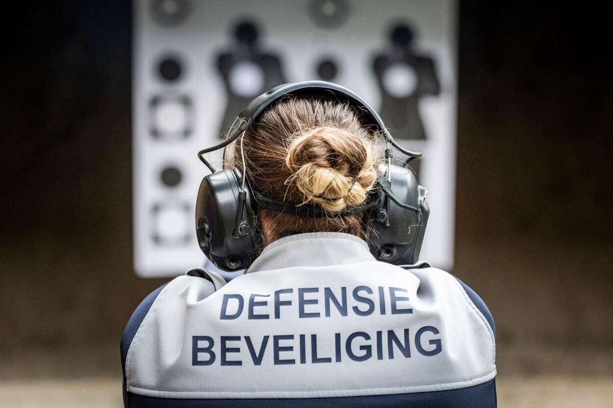 Een vrouwelijke collega van Defensie Beveiliging op de rug gezien met headset op. Ze richt haar pistool op een doelwit.