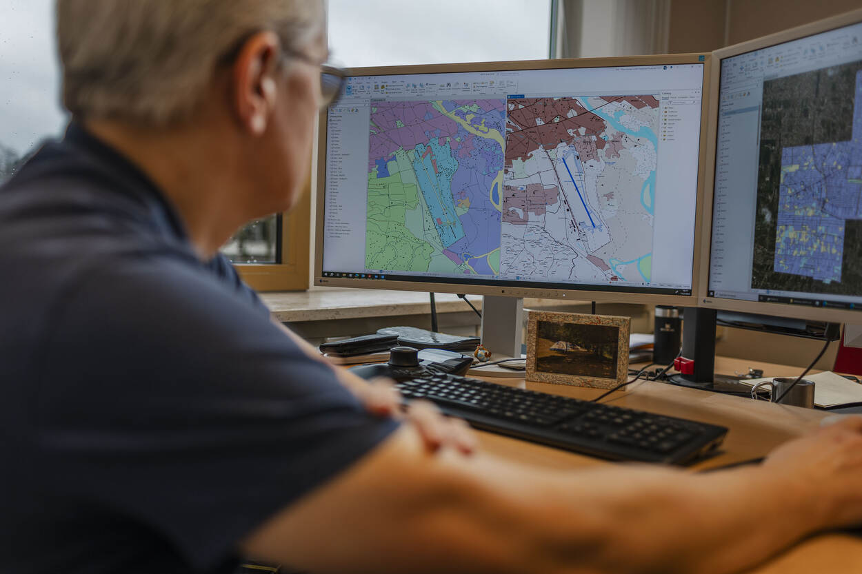 Een medewerker van de Dienst Geografie zit achter zijn computer en laat een kaart zien.