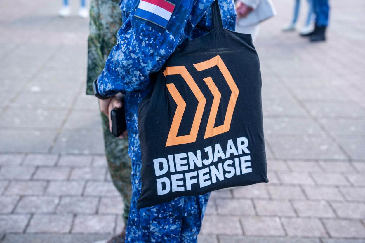 Marinecollega’s in blauwe camouflagepak houdt een tas vast met daarop de tekst Dienjaar Defensie.