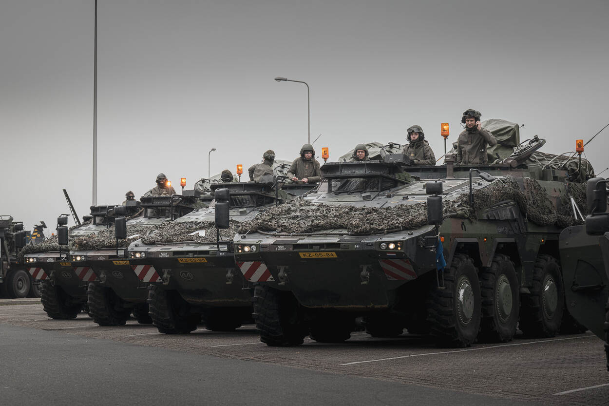 Legervoertuigen naast elkaar geparkeerd. In elk voertuig staan 2 militairen rechtop.