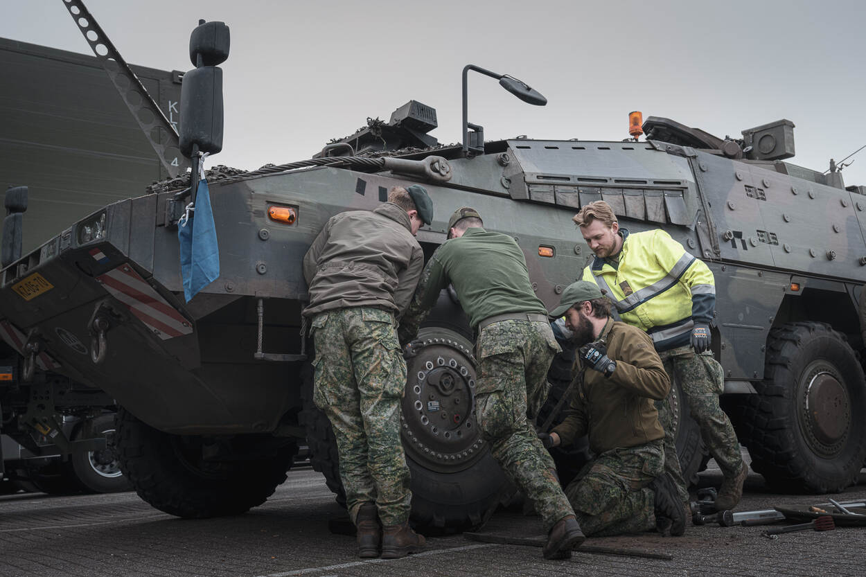 4 militairen werken aan de linker voorband van een militair voertuig.