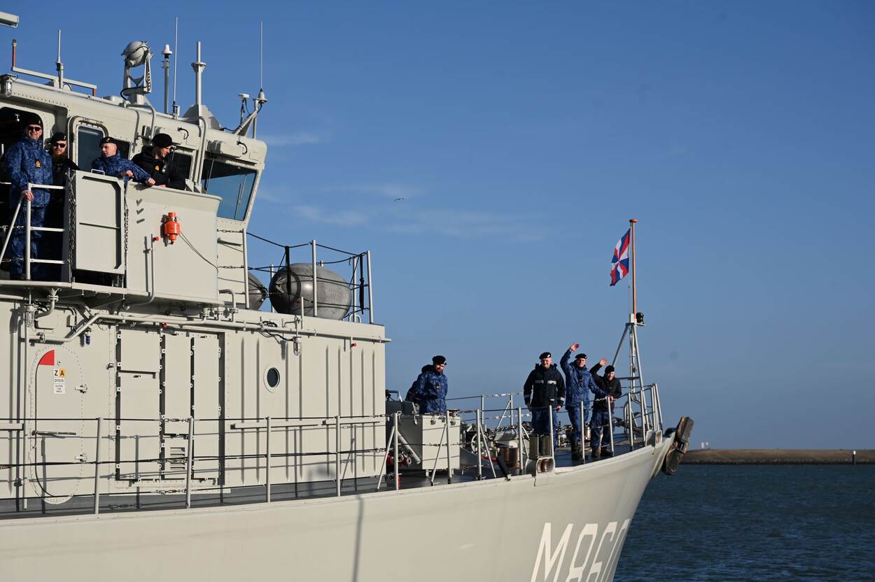 Een marineschip op zee met zwaaiende bemanningsleden.