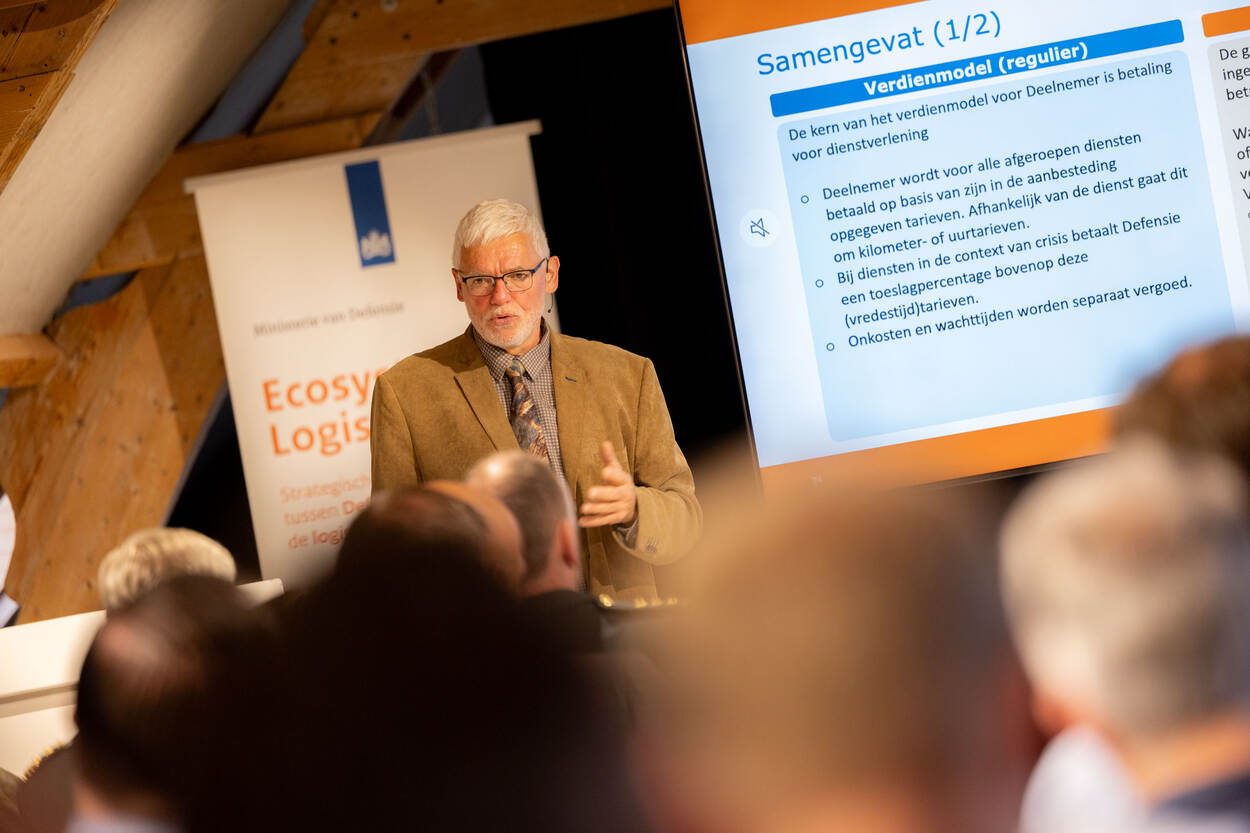 Een man spreekt een zaal toe.