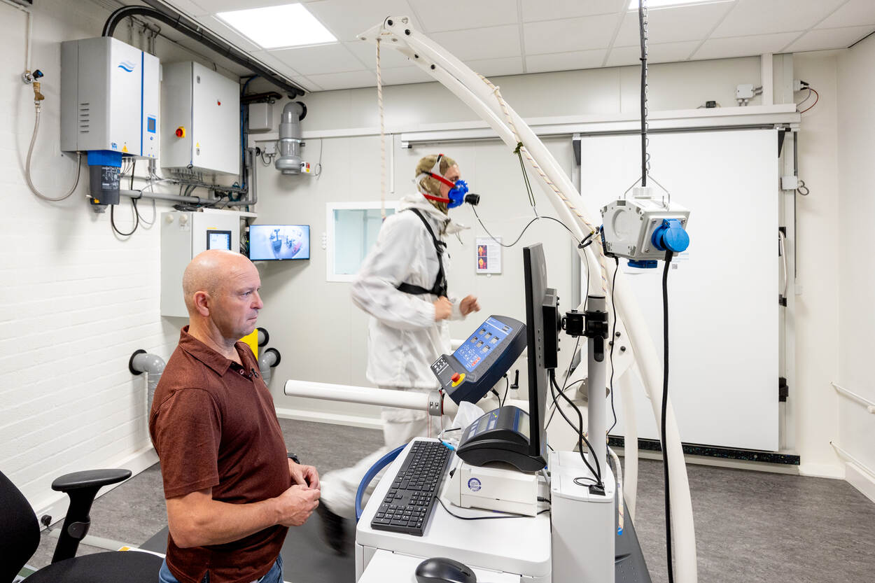 Gerard staat achter een computer en kijkt aandachtig naar het scherm. Naast hem rent een militair op een loopband met een zuurstofmasker op. Op de achtergrond is de klimaatkamer te zien.