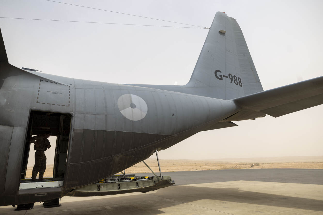 Staartdeel van een C-130 transportvliegtuig met laadklep omlaag. In deuropening staat iemand van de bemanning.