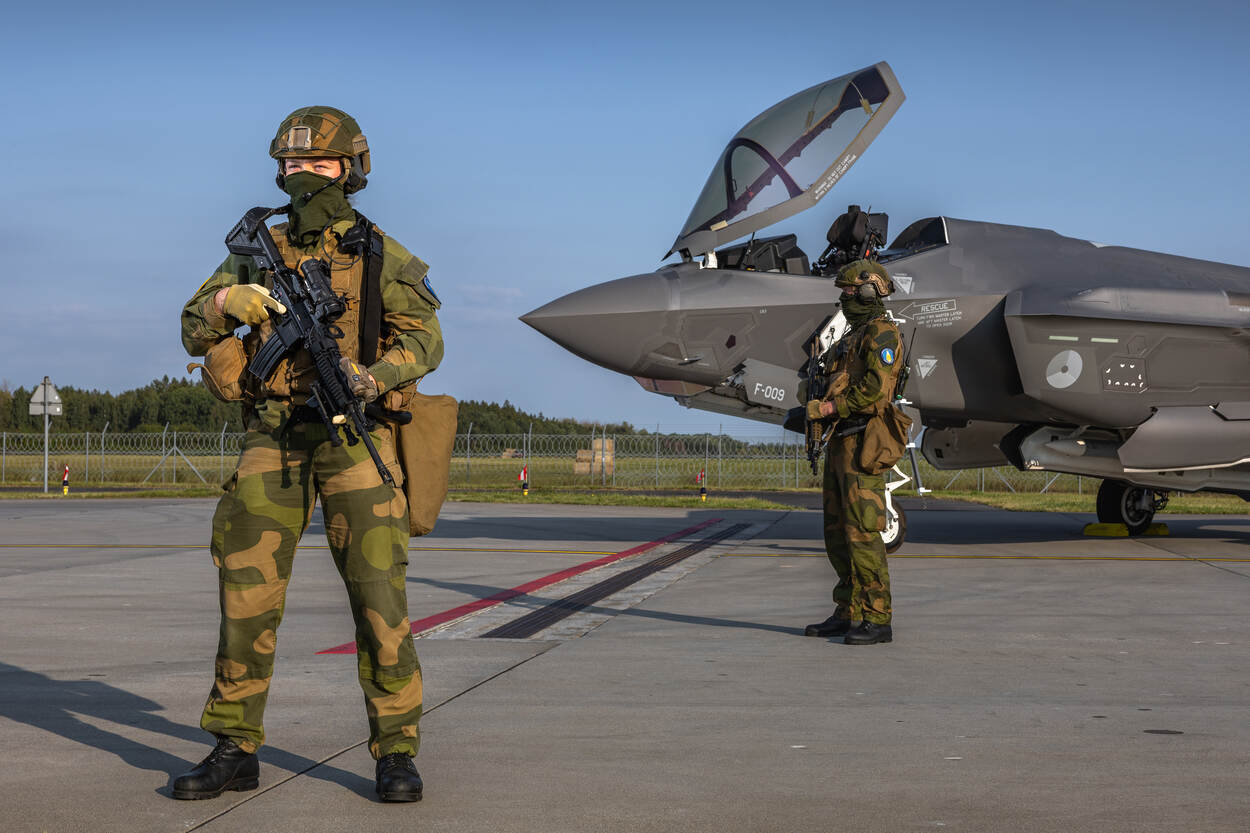 Twee Noorse militairen in vol ornaat met wapen staan voor een F-35.