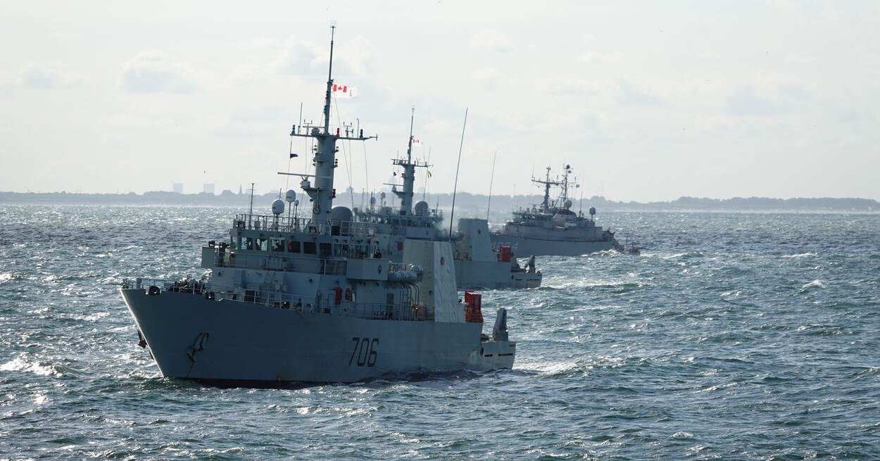 Op volle zee bij Scheveningen varen drie mijnenbestrijdingsvaartuigen achter elkaar.