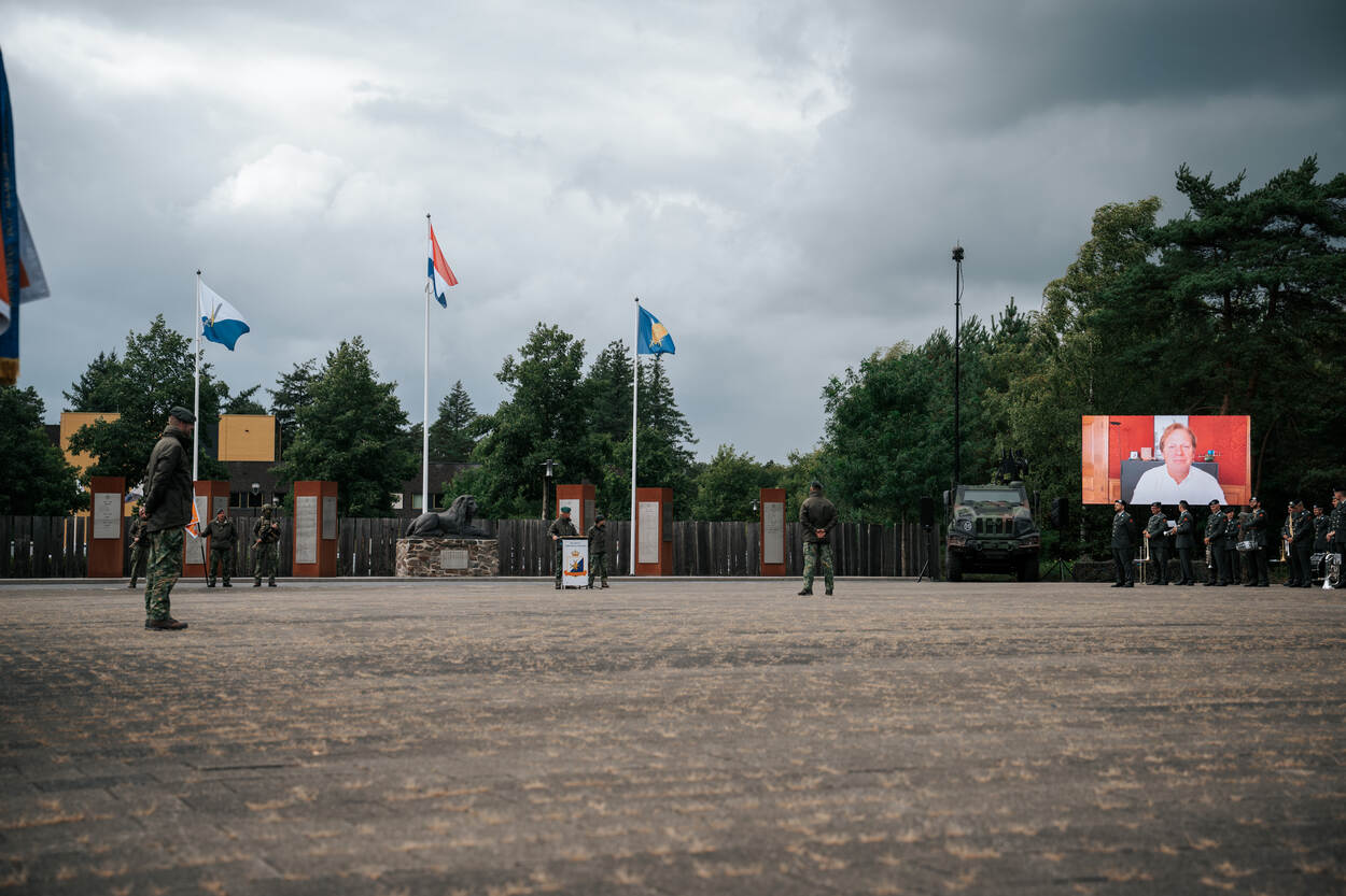Op een groot scherm spreekt de staatssecretaris van defensie Gijs Tuinman de aanwezigen toe.