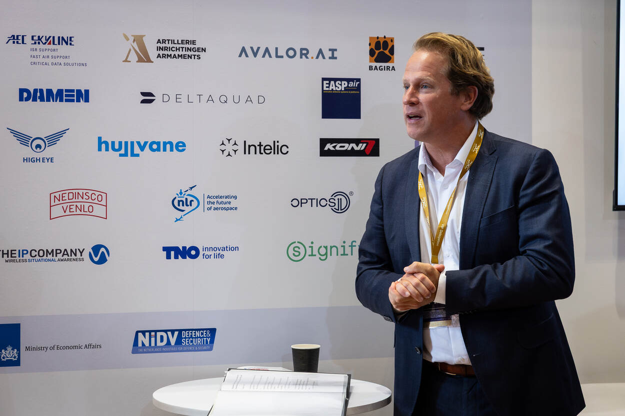 Staatssecretaris Gijs Tuinman spreekt de ondernemers toe, vlak voor het bord met alle deelnemers aan de Oranje Paviljoen op de DSEI.