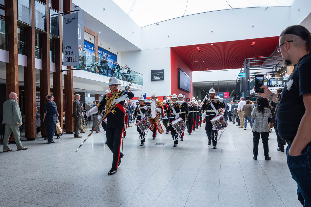 Overzicht van de beursvloer in een van de 22 hallen. Een muziekkorps loopt over de boulevard.