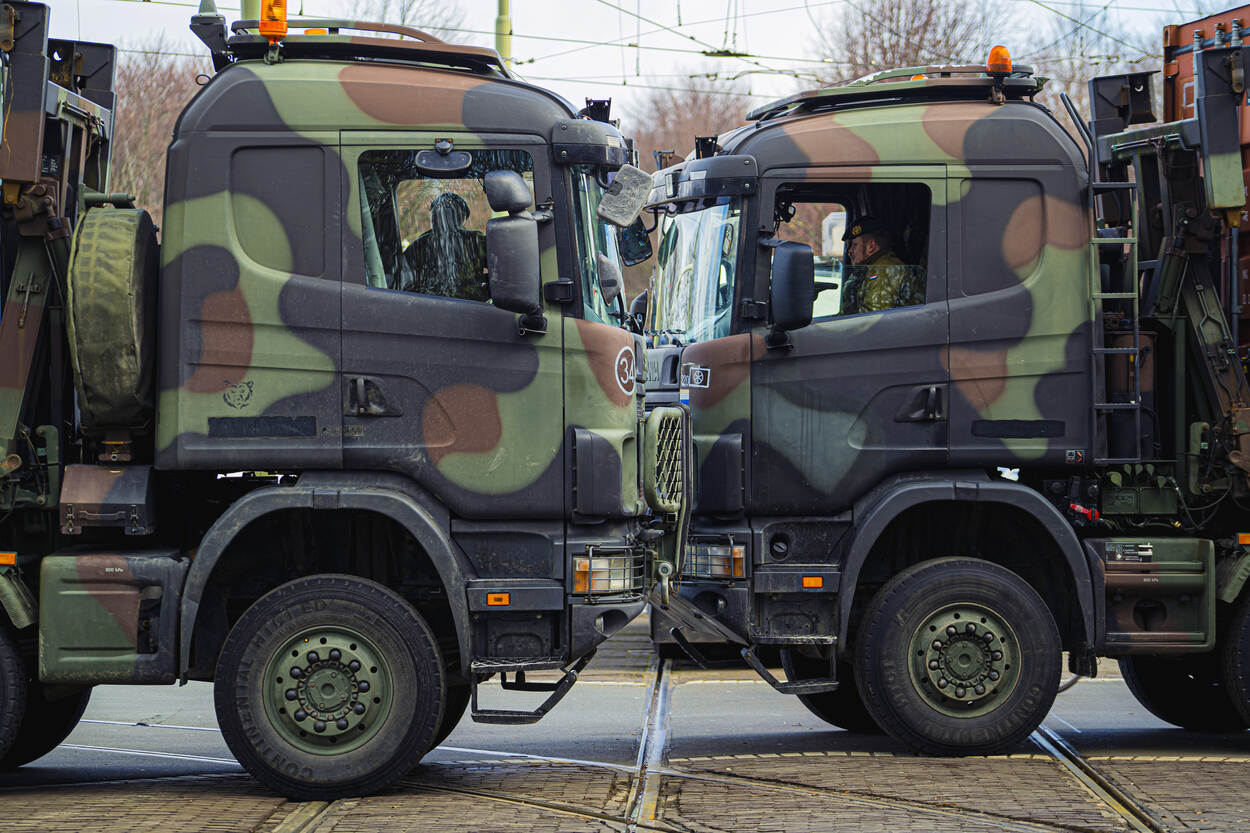 Twee militaire vrachtwagens staan neus aan neus in Den Haag, dwars op de trambaan.