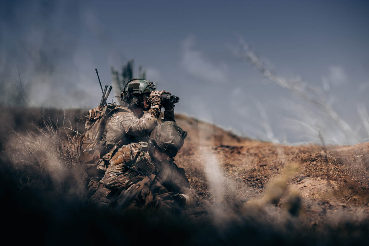 2 militairen, van wie er 1 door een verrekijker tuurt.
