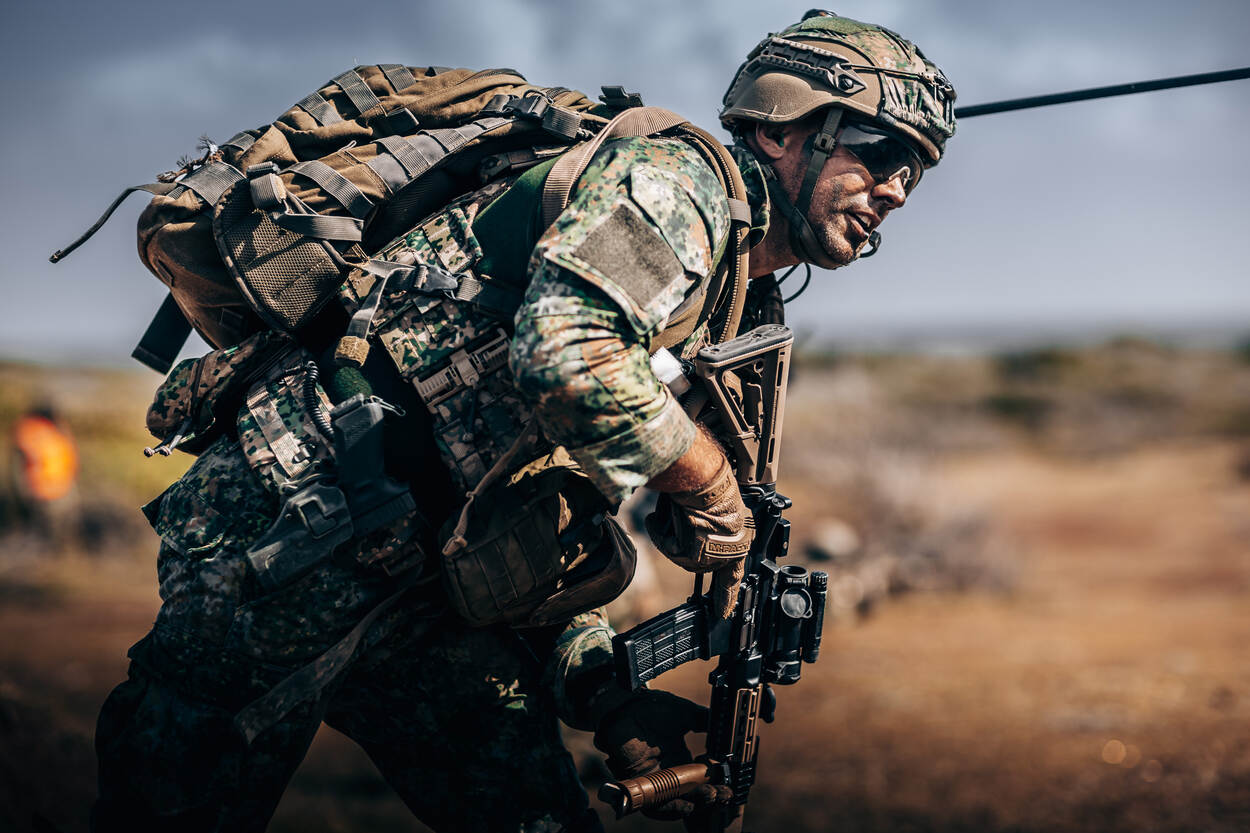 Een marinier gaat met een ingespannen trek op het gezicht gekromd voorwaarts.