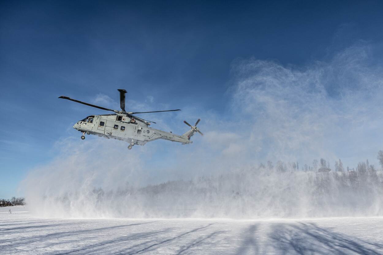 Een NH90 maakt een landing in de sneeuw die hoog opwaait.