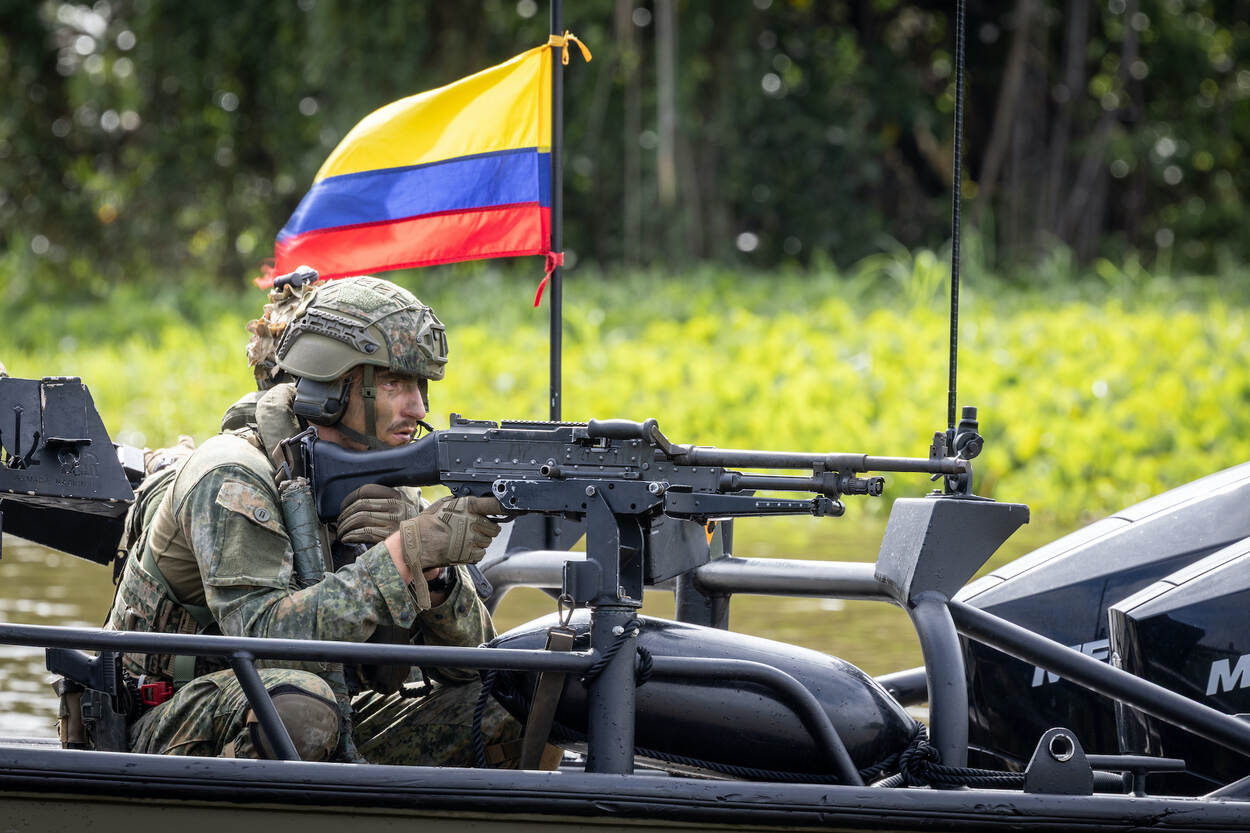 Een marinier zit op een bootje achter een MAG-machinegeweer, op de achtergrond de Colombiaanse vlag.