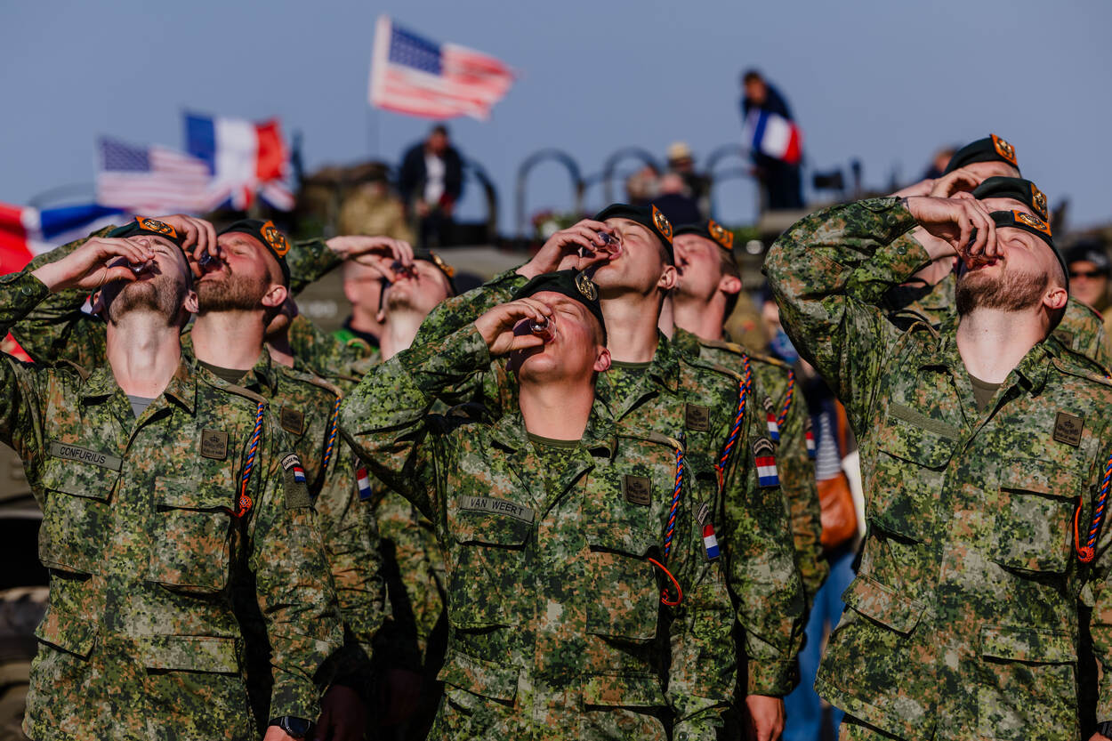 Een groepje fuseliers slaat tegelijkertijd een klein, plastic glaasje met oranjekleurige drank achterover.