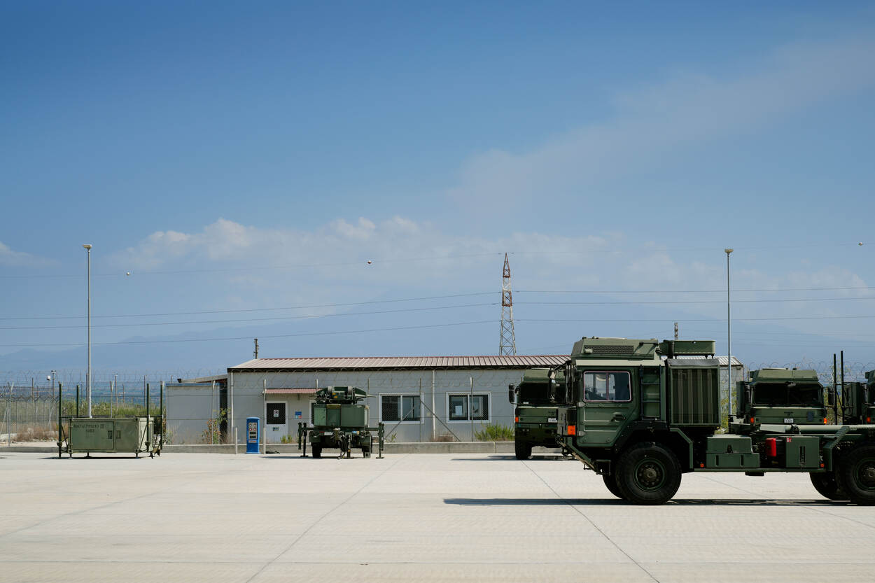 Er komt rook uit de Etna, met op de voorgrond een voertuig van de NISRF op en verder lege parkeerplaats.