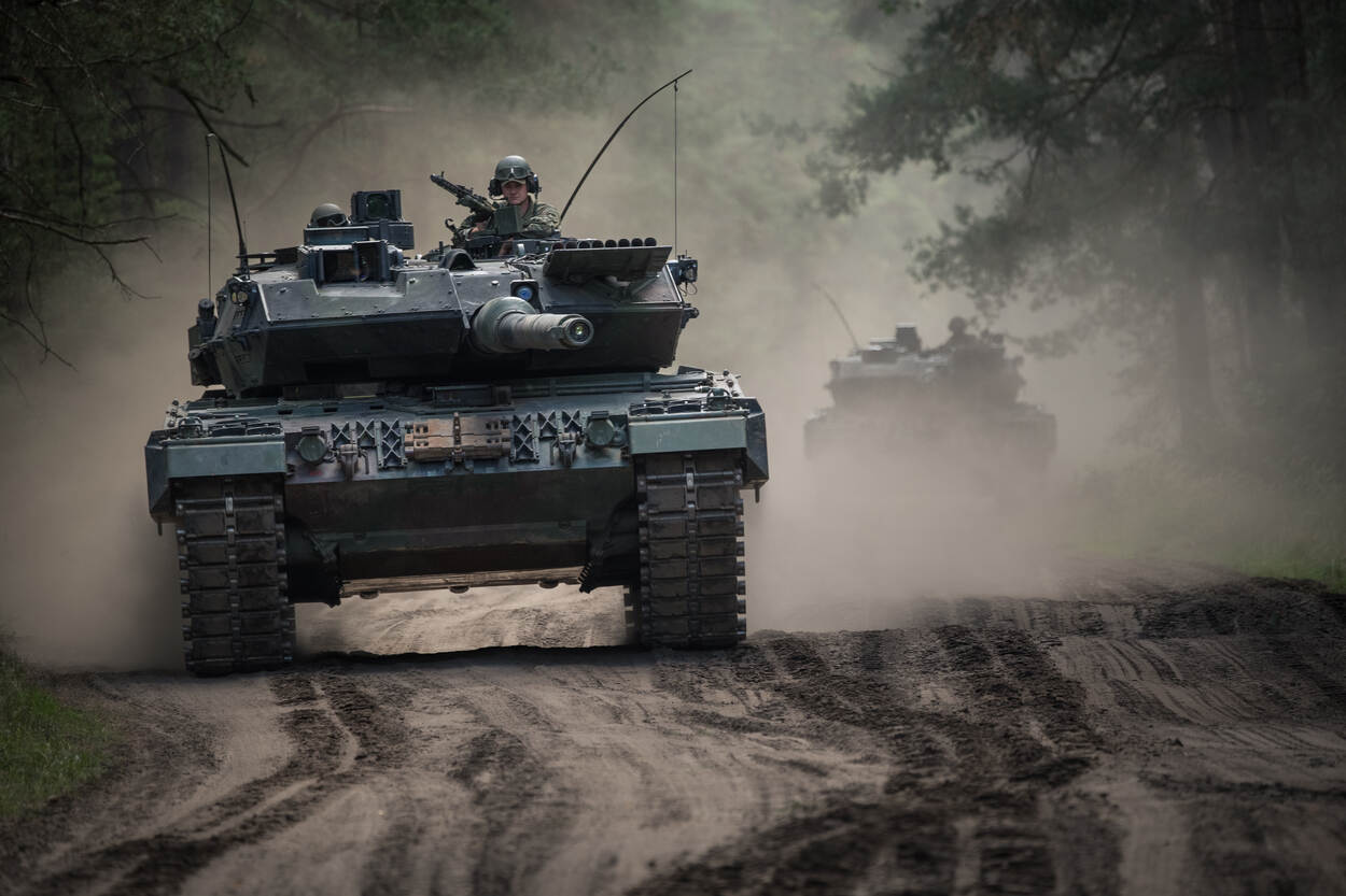 Een leopard-gevechtstank rijdt door het oefenterrein en creeert een stofwolk, met een andere Leopard rijdend in de kielzog.