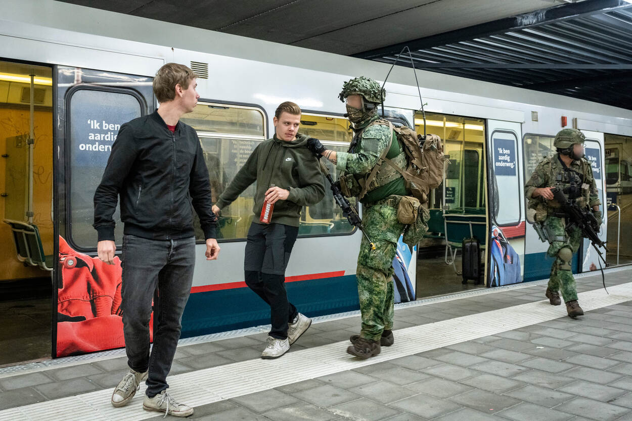Een militair begeleidt twee metropassagiers de metro uit, op het fictieve perron in Vught.