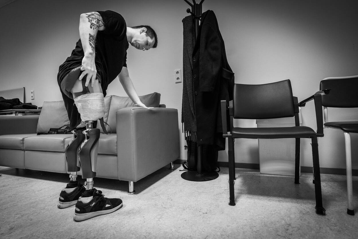 De Oekraïense Illia houdt zich vast aan een bank terwijl hij zijn rechterstomp goed in de beenprothese stopt.