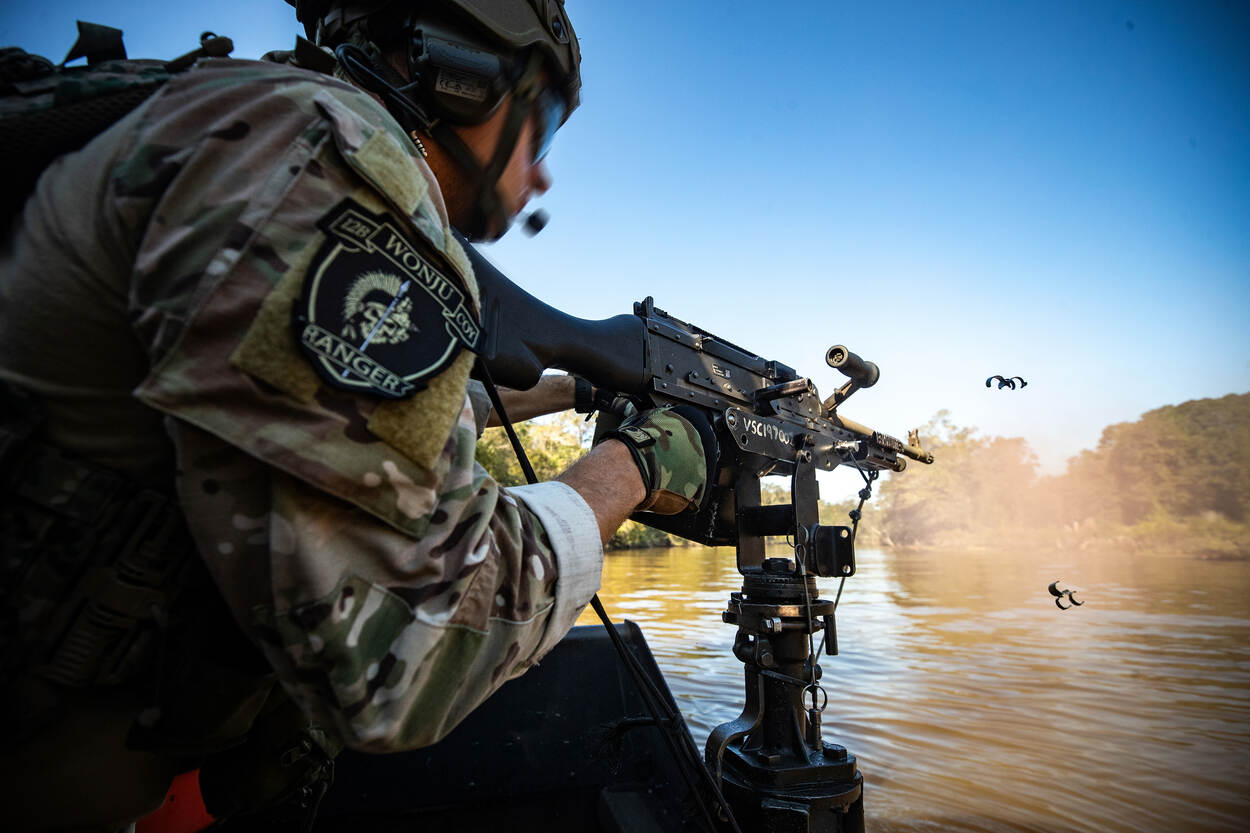 een militair in een boot op een rivier vuurt met zijn wapen.