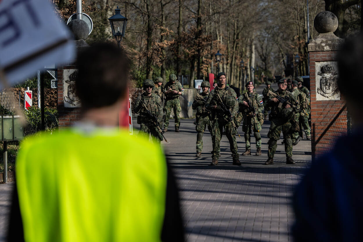 Groepje demonstranten met spandoeken staat bij ingang oog in oog met gewapende militairen