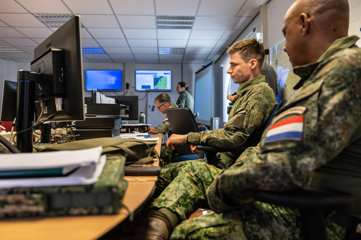 Militairen zitten naast elkaar achter een scherm.