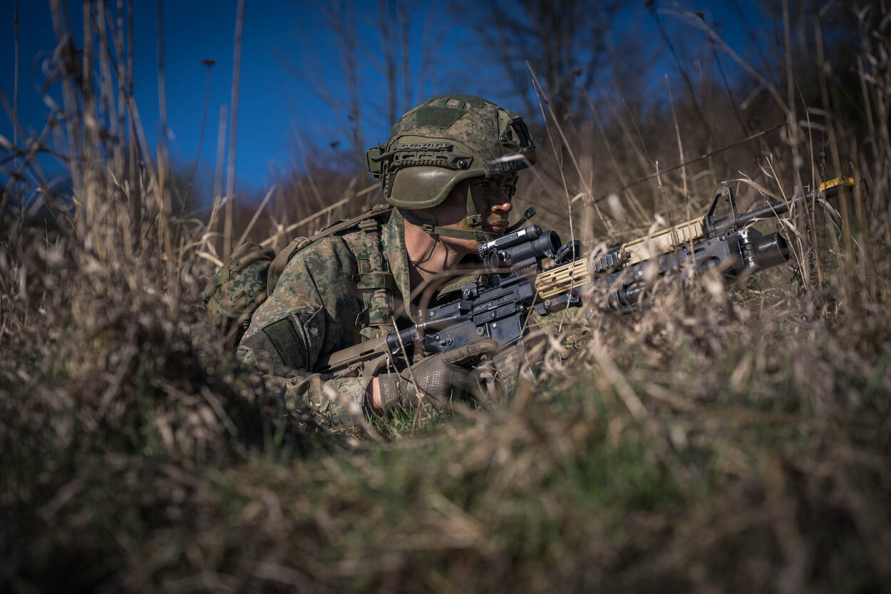 Een militair ligt in het gras en vecht heuvelopwaarts.