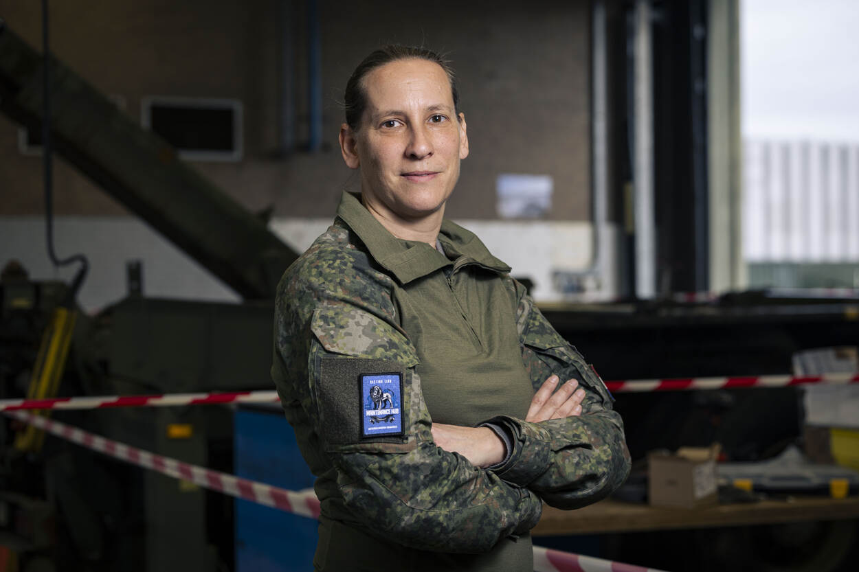 Een militair met armen over elkaar poseert in een garage met daarachter rood-witte linten.