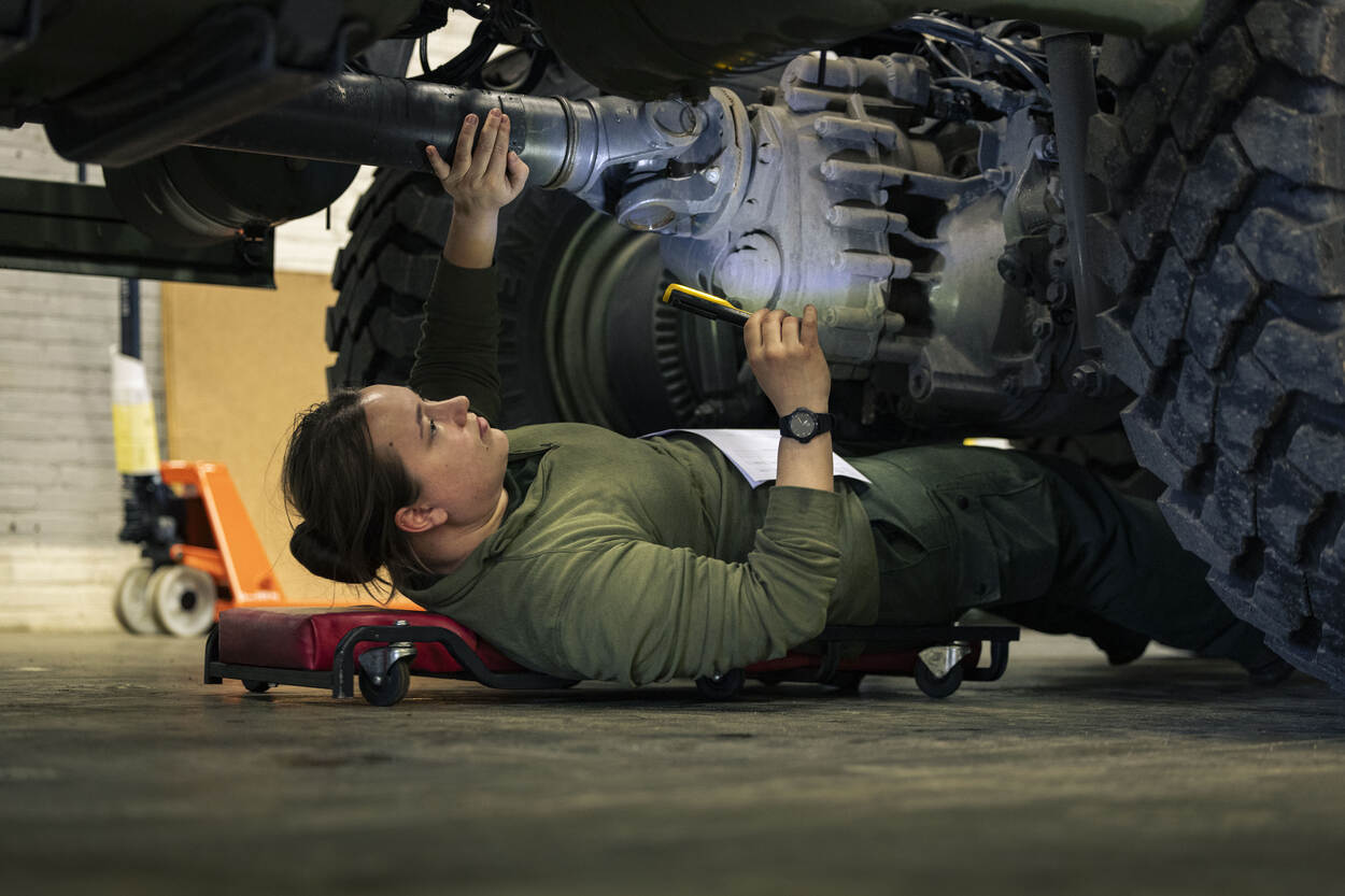 Een vrouwelijke monteur ligt in garage onder een militair voertuig om te sleutelen.