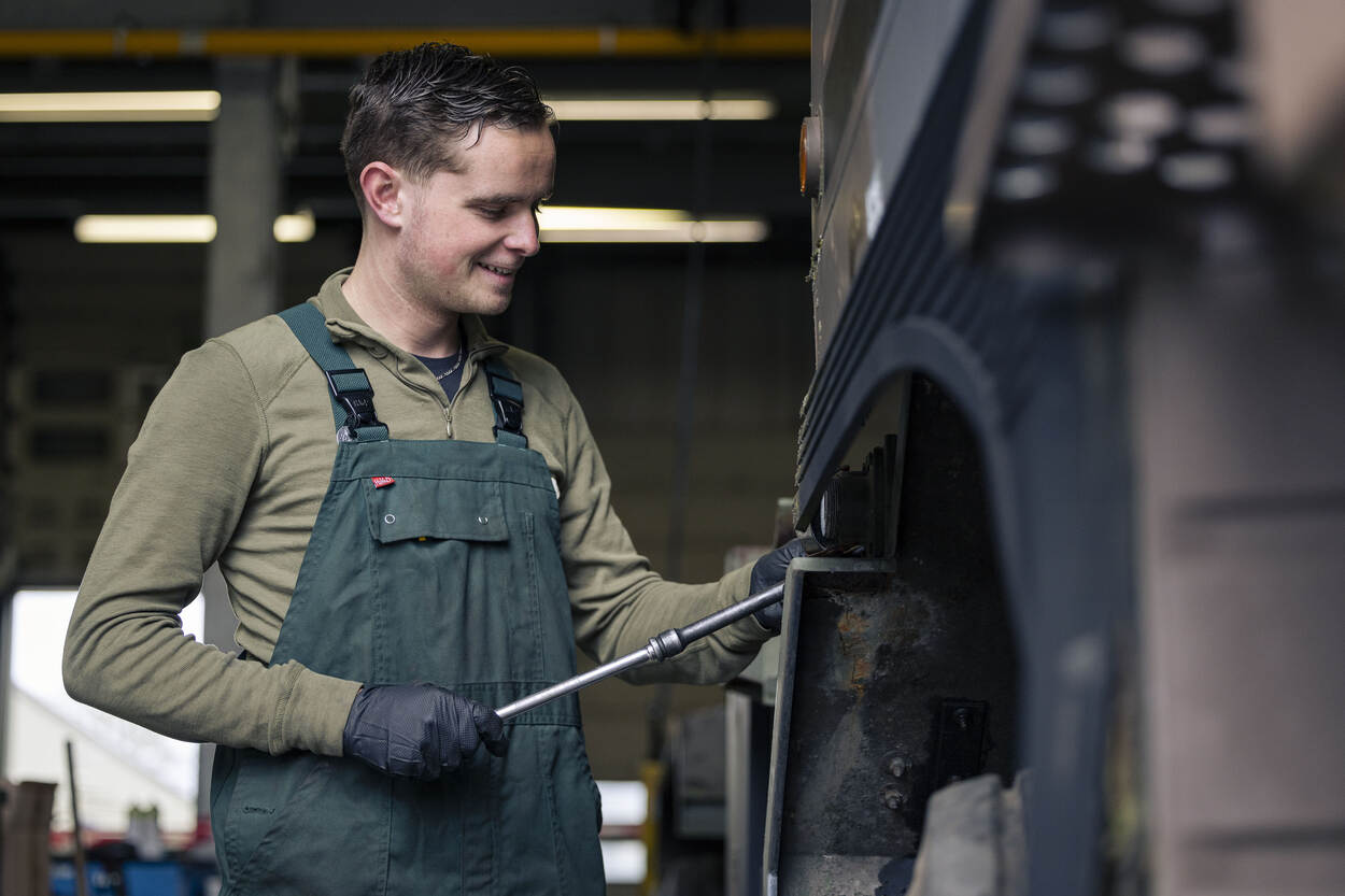 Een medewerker in overall sleutelt aan een militaire vrachtauto.