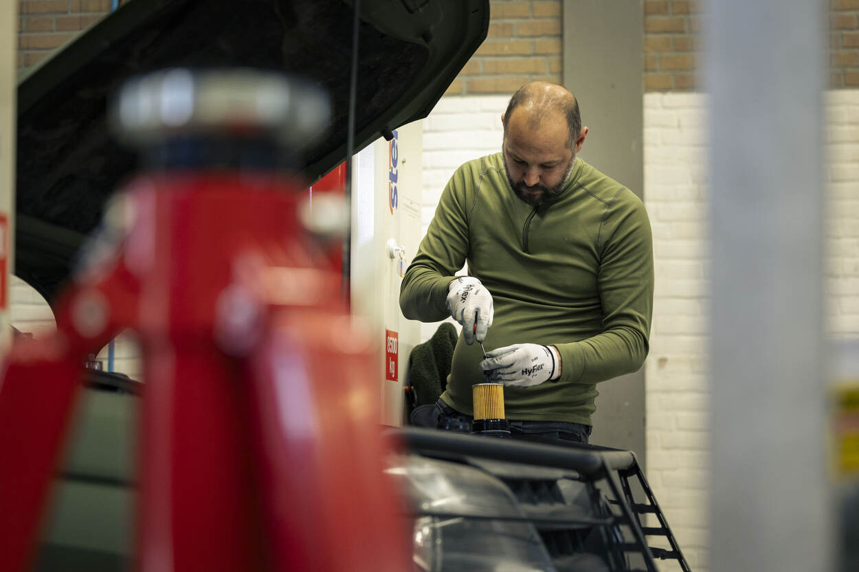 Een medewerker hangt boven een militair voertuig en roert in een potje.