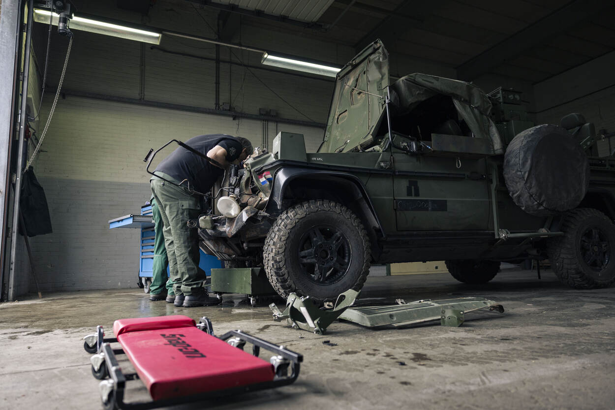 Een medewerker hangt in een garage boven de motor van een militair voertuig.