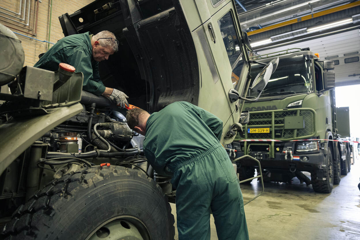 2 medewerkers checken een militair voertuig, terwijl de cabine omlaag hangt.