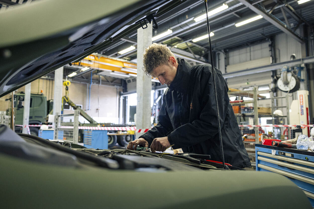Een medewerker zit met zijn handen aan de bedrading van een militair voertuig met de klem open.