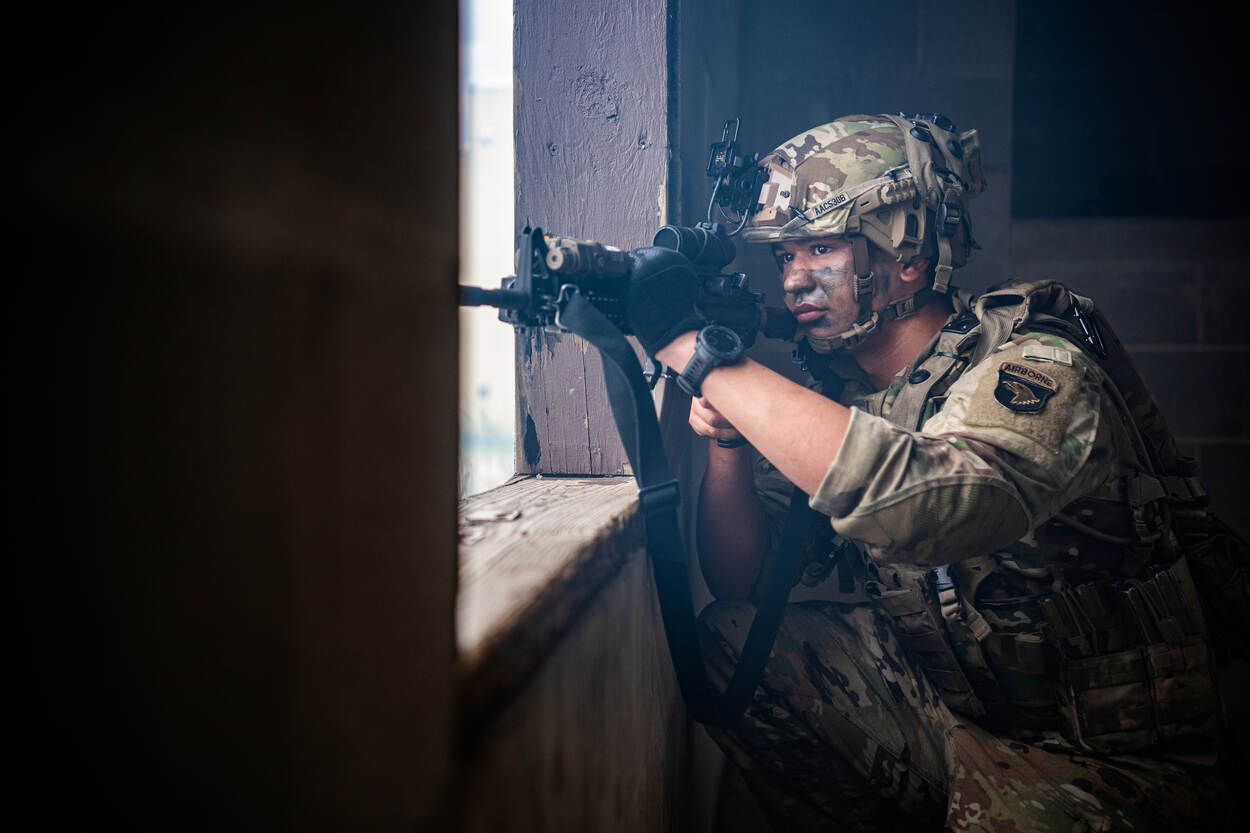 Foto links: een militair kijkt door een raam van een gebouw naar buiten, met zijn lange wapen voor het gezicht. Rechts: een drone vliegend in de lucht.