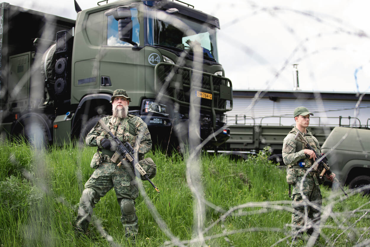 Twee militairen met een vrachtwagen op de achtergrond.