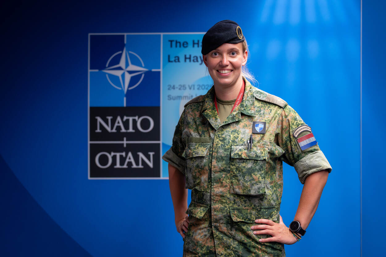 Vrouwelijke luitenant met baret poseert voor logo NAVO-top.