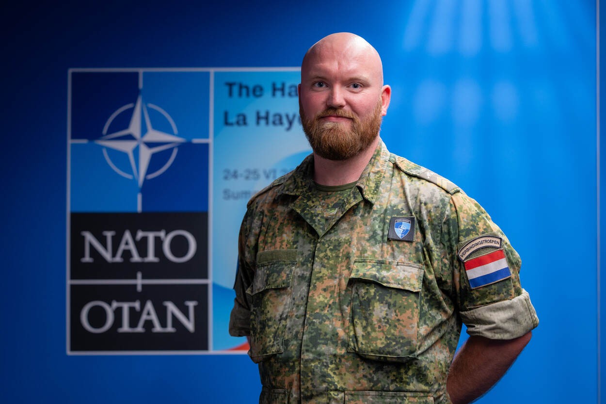 Mannelijke militair zonder baret poseert voor logo NAVO-top.