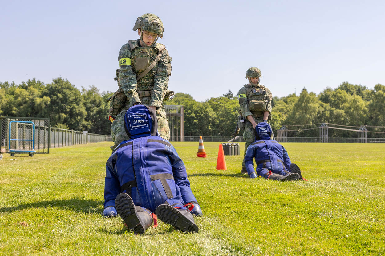 Twee militairen verslepen poppen over het grasveld.