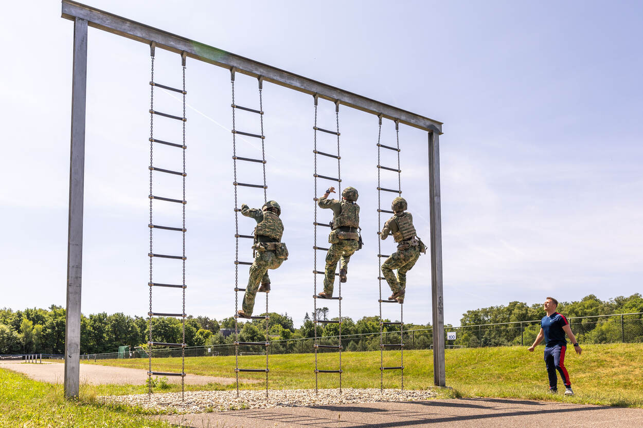 Drie militairen klimmen een touwladder omhoog.