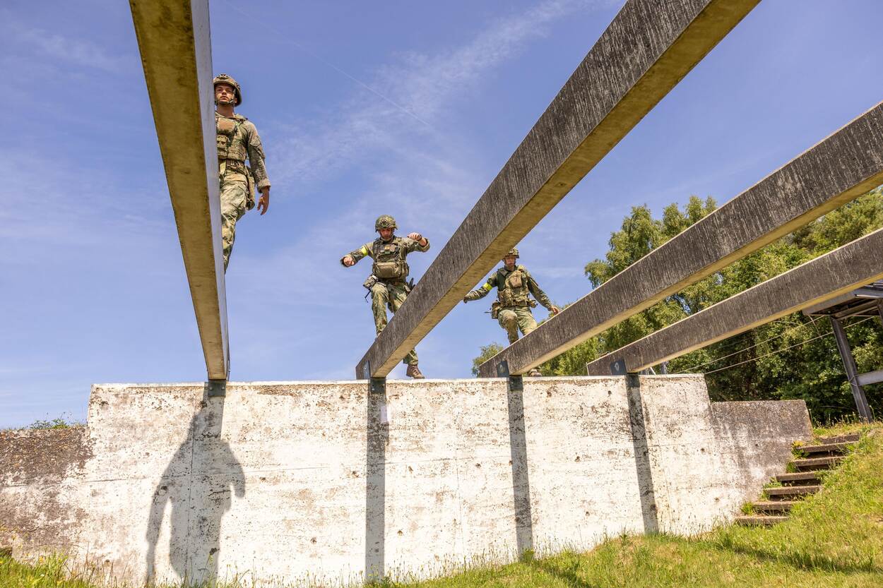 3 militairen lopen over evenwichtsbalken.